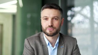 İş yerinde iş yerinde oturan mutlu iş adamının portresi. Kameraya bakarak poz veren başarılı gülümseyen girişimci. Yakışıklı sakallı menajerin ya da işçinin kafa resmi. Kapat.