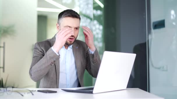 ストレスを受けたビジネスマンは ビジネスオフィスの職場に座っている間 ノートパソコンで悪いニュースを読みます スーツの労働者の失望した男は コンピュータ上の否定的な情報をレビューすることに動揺しています — ストック動画