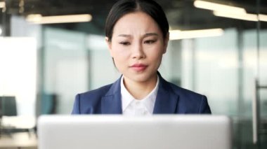 Kafası karışmış Asyalı iş kadını iş yerinde dizüstü bilgisayar kullanmakta zorlanıyor. Kafası karışmış kadın işçinin bilgisayardaki uygulamayla ilgili karmaşık sorunları var. Kapat.