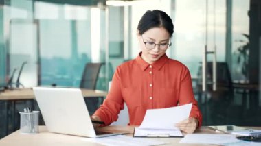 İş yerinde çalışırken dizüstü bilgisayarla evrak işleriyle uğraşan Asyalı genç bir muhasebeci. Gözlüklü kadın finansör mali rapor hazırlıyor ya da vergi formu yazıyor.