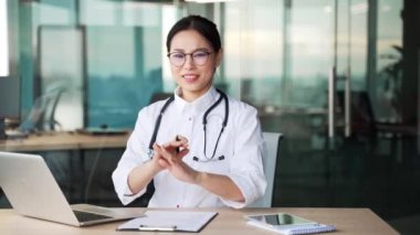 Beyaz önlüklü Asyalı kadın doktor kollarını çapraz gösteriyor, X işareti, hastane kliniğinde otururken başını sallıyor. Tıp doktoru bir yasaklama, inkar, anlaşmazlık jesti gösteriyor.