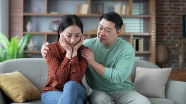 Asyalı koca evdeki oturma odasında kanepede otururken acı çeken karısını teselli ediyor. Şefkatli adam üzgün kadına sarılıp destek veriyor. Kavgadan ya da sorunlardan sonra üzgünüm, depresyon ve kriz