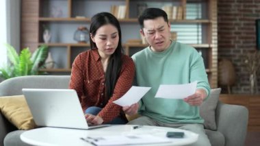 Asyalı evli çiftin evde dizüstü bilgisayar kullanarak faturalara bakması hayal kırıklığı yarattı. Maaş çeki tutan üzgün bir adam. Karışık karı koca ev işlerinde zorlanıyorlar.