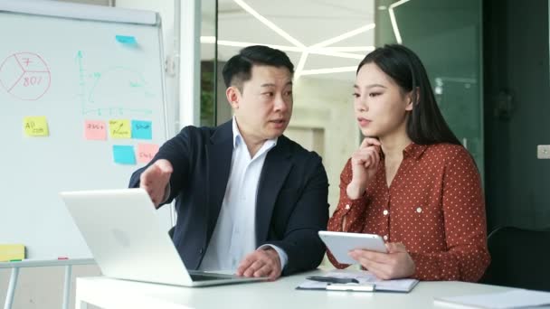アジアのボスは ビジネスオフィスの職場で若い女性労働者に相談します 男性マネージャーは 開発プロジェクトについて従業員と話すことをアドバイスします エグゼクティブは ラップトップコンピュータを使用して作業上の問題を説明します — ストック動画