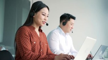Müşteri desteği için çalışan Asyalı şirket yöneticileri dizüstü bilgisayar kullanarak bir video görüşmesi yapıyorlar. Telsiz kulaklık takmış çağrı merkezi ajanları, kadınlar ve erkeklerden oluşan bir ekip. Çevrimiçi danışma