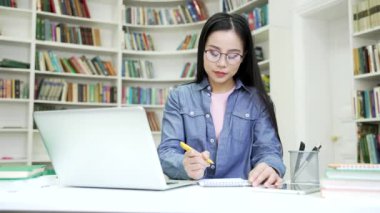 Asyalı kız öğrenciler kampüs kütüphanesinde dizüstü bilgisayar kullanarak ders çalışırlar. Uzaktan öğrenim seminerindeki genç kadın üniversitede online e-öğrenme, video kursu veya konferans dinliyor