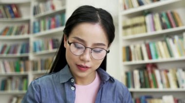 Asyalı kız öğrenci kitap okuyarak, üniversite kütüphanesinde notlar alarak ders çalışıyor. Gözlüklü genç bir kadın muayene döneminde öğreniyor. Başvuru sahibi giriş sınavları için hazırlanır. Kapat.