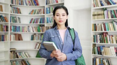 Kampüs kütüphanesinde elinde kitaplarla duran kendinden emin Asyalı kız öğrencinin portresi. Sınıfta ciddi bir genç kadının vesikalık fotoğrafı. Kamera pozu veren düşünceli bir başvuru sahibi.