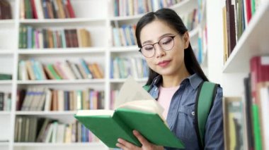 Odaklanmış Asyalı kız öğrenci üniversite kütüphanesinde kitap okumayı öğreniyor. Genç kadın sınıfta sınav dönemi için çalışıyor. Başvuru sahibi giriş sınavları için hazırlanır. Kapat.