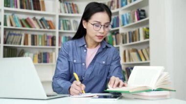 Asyalı kız öğrenci kitap okuyarak, kampüs kütüphanesinde notlar alarak ders çalışıyor. Genç bir kadın üniversitede sınav döneminde öğreniyor. Başvuru sahibi giriş sınavları için hazırlanır