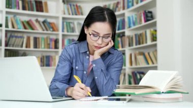Üniversite kütüphanesinde ev ödevi yapmaktan sıkılmış Asyalı bir kız öğrenci. Yorgun kız öğrenme, yazma, sınav döneminde okuma. Çok çalışan aday giriş sınavları için hazırlanıyor