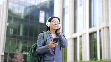 Asyalı mutlu bir kız öğrenci, üniversite binası yakınlarında kampüs çevresinde dolaşırken kulaklık takarak müzik dinliyor. Genç bir kadın şarkı listesine girer ve en sevdiği parçayı sever.