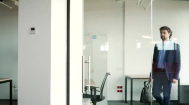 Resmi takım elbiseli sakallı bir işadamı modern bir binada cam bir kapı açıyor ve ofisten koridora çıkıyor. Elinde evrak çantası olan bir girişimci ya da işçi iş yerinden ayrılıyor.