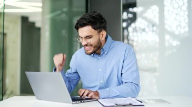 Mutlu iş adamı iş yerinde otururken dizüstü bilgisayarından harika haberler aldı. Gülümseyen işçi bilgisayarda hoş bir mesaj okur, başarıyı kutlar, galibiyete sevinir