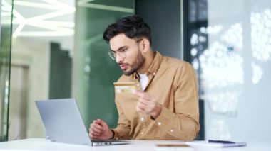 Şok olmuş girişimci, iş yerindeki iş yerinde oturan bilgisayarından kredi kartını kontrol ediyor. Sinirli işçi dolandırıcılıkla yüzleşti, hesabından para çalındı. İnsanoğlu aldatılmanın kurbanı oldu.