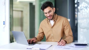 Finansör, iş yerindeki masada oturan dizüstü bilgisayarla form doldurmakla meşgul. Ciddi odaklı muhasebeci adam mali rapor hazırlıyor.