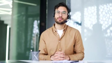 Webcam görüntüsü. Ofiste kameraya bakan kendine güvenen bir yönetici konuşuyor. Telsiz kulaklıklı iş adamının bir iş görüşmesi var, uzaktan konuşuyor, online konferansta iletişim kuruyor.