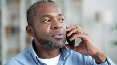 Kendinden emin, Afro-Amerikan bir adam akıllı telefonuyla konuşuyor. Oturma odasındaki kanepede oturuyor. Kıdemli sakallı iş adamı bir iş ortağı ya da müşterisiyle iletişim kurar.