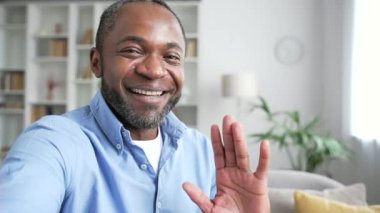 POV Olgun Afro-Amerikalı bir adam video konuşmasında akıllı bir telefonla konuşuyor. Evdeki oturma odasındaki kanepede oturan kameraya bakıyor. Gülümseyen kıdemli işadamı iş ortağıyla internette sohbet ediyor.