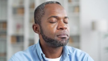 Ciddi bir Afro-Amerikan erkek portresi. Ev ofisinin oturma odasındaki kanepede oturuyor. Kendine güvenen bir iş adamının kafasından. Yaşlı sakallı siyah adam kameraya bakarak poz veriyor. Kapat.