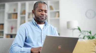 Ev ofisinin oturma odasında kanepede otururken dizüstü bilgisayarda yazan Afro-Amerikan erkek arkadaşın kutlu olsun. Freelancer bilgisayarda uzaktan çalışıyor. Yaşlı sakallı siyahi adam internette sohbet ediyor.