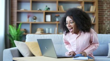 Genç, mutlu, Afro-Amerikan kadın laptopta harika haberler okuyup merkez ofisteki koltukta otururken şok oldum. Heyecanlı siyahi kadın serbest yazar başarıyı kutluyor, bilgisayardaki olumlu mesajla tatmin oluyor.