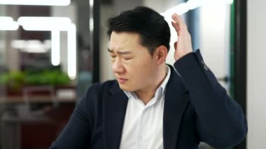 İş yerindeki masasında otururken boynu ağrıyan Asyalı hasta işadamı. Yorgun ve çalışkan bir erkek işçi resmi bir takım elbise giyer, masaj yapar ve ağrıyan kasları ovuşturur.