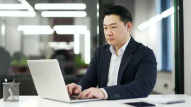 İş yerindeki bir iş yerinde dizüstü bilgisayarda yazan Asyalı bir işadamı. Bilgisayar uygulamalarında çalışan, bankacılık yapan, müşteriye mesaj atan, internette sohbet eden resmi bir girişimci. bir proje ile meşgul