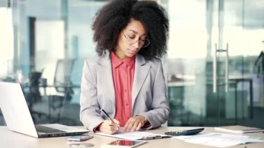Genç Afro-Amerikan kadın muhasebeci ya da finansör iş yerindeki iş yerinde oturan bir kalemle belgeleri dolduruyor. Siyahi kadın, hesap makinesi kullanarak finansal hesaplamalarla uğraşıyor.