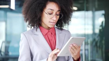Ceketli Afro-Amerikan iş kadını, iş yerinde dijital tablet kullanıyor. Siyahi bir kadın mesaj yazıyor, müşteriyle sohbet ediyor ya da internette geziniyor. Kapat.