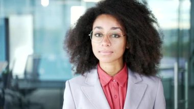 Takım elbiseli Afro-Amerikan bir iş kadınının iş yerinde duran portresi. Gözlüklü ciddi bir zenci kadın kameraya bakıyor. Bayan öğretmenin vesikalığı. Kapat.