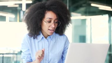 İş yerindeki bir iş yerinde dizüstü bilgisayarla konuşan Afro-Amerikan kadın bir çalışan. Siyahi bir kadın internet konferansında iletişim kurar ya da bir müşteriyle sohbet eder. Kapat.