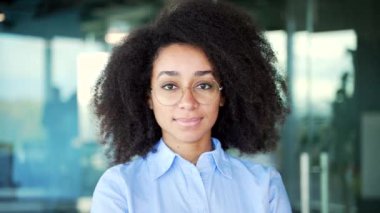 İş yerinde mavi gömlekli mutlu bir Afro-Amerikan kadın çalışanın portresi. Gözlüklü, gülümseyen siyah kadın kameraya bakıyor. Pozitif bir işçinin vesikalığı. Kapat.