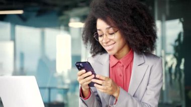 Heyecanlı genç Afro-Amerikan iş kadını iş yerindeki iş yerinde telefonda harika haberler okuyor. Siyahi kadın başarıyı kutlar, galibiyetle sevinir, gülümser, evet işareti yapar.