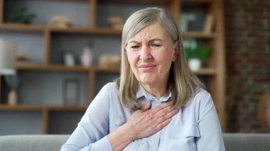 Son sınıf öğrencisi, gri saçlı, mide ekşimesinden muzdarip. Evdeki oturma odasında, kanepede oturuyor. Hasta, yaşlı bir kadın elini göğsüne dayayıp acı çekiyor, karnında yanıklar var. Kapat.