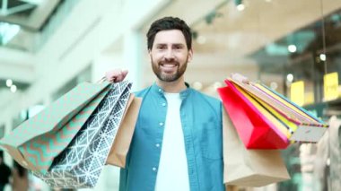 Alışveriş merkezindeki yakışıklı bir adamın portresi mağazadaki kamera çantalarını gösteriyor. İndirim ve satış yapan memnun erkek müşteriler.