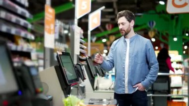 Erkek müşteri süpermarkette kasiyer kasiyeri kullanıyor. Alışveriştekiler, bakkalda kasiyer olarak kullandıkları ürünleri tarıyorlar. Kasiyer terminali çalışanı ürünlere online ödeme yapıyor.