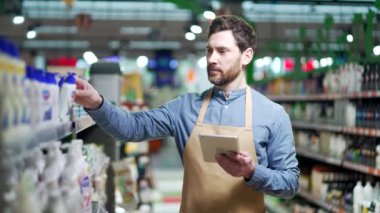 Tablet üzerinde çalışan yakışıklı bir çalışan, kozmetik raflarının yanında duran ürünlerin durumunu kontrol eden yönetici süpermarkette ya da hipermarkette ürün listesi envanteri yazıyor.
