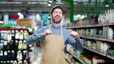 Pazar yerinde dans eden neşeli süpermarket satıcısı. Önlüklü mutlu komik adam marketteki rafların arasında iş yerinde seviniyor Neşeli çalışan ya da sahibi