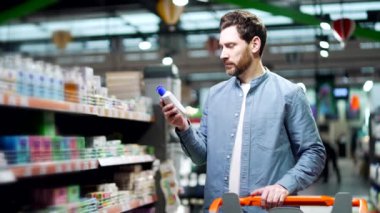 Adam ürününün bileşimini Süpermarkette Kozmetik Şişesi 'ndeki şampuan Erkek Müşteri Etiketi' nde inceliyor. Çalışmalar bilgi toplar ve okur. Markette seçimler yapanlar göz önünde bulundurulur.