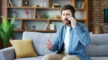 Evdeki oturma odasında koltukta oturmuş cep telefonuyla tartışan sinirli, heyecanlı bir adam. Sinirli, olgun, sakallı erkek akıllı telefondan çözülmesi gereken sorunlar hakkında çığlıklar atıyor.