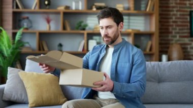 Mutsuz adam, evdeki oturma odasında kameraya bakarak yanlış ürünle dolu bir paket aldı. Sakallı erkek, online mağazadan alışveriş yapmaktan memnun değil. Servis sorunu. Hasarlı öge