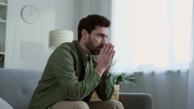Depresyon ve zihinsel acıdan muzdarip üzgün bir erkek evdeki oturma odasında kanepede oturuyor. Yalnız sakallı adam sorunlarını düşünüyor. Mutsuz, hayal kırıklığına uğramış, kötü bir ruh hali içinde, endişeli.