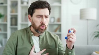 Boğazı ağrıyan hasta bir adam, evdeki oturma odasında kanepede otururken öksürüyor. Sakallı bir adam boğazına sprey sıkar. Tedavici soğuk algınlığı, virüs ya da grip. Kapat. 