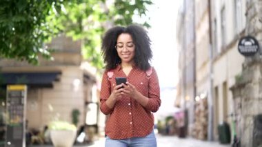 Mutlu Afro-Amerikan genç bayan turist akıllı cep telefonuyla geziyor açık havada gülümseyen siyah kız öğrenci internet hayat tarzı seyahat ve seyahat konseptine giriyor.