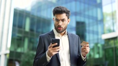 Şok olmuş işadamı, bir iş yeri binasının yakınındaki bir sokakta telefonla kredi kartını kontrol ediyor. Hüsrana uğramış işçi dolandırıcılıkla yüzleşti, hesabından para çalındı. Aldatılmaya kurban gitti.