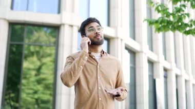 Yakışıklı sakallı iş adamı cep telefonuyla konuşuyor caddede ofis binasının yanında duruyor. Gülümseyen başarılı bir girişimci müşterisiyle iletişim kurar ya da iş ortağıyla sohbet eder.