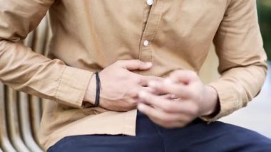 Kapatın. Erkek el, karın masajı yapıyor. Gömlekli bir adam iş yerinin yakınındaki bir bankta otururken mide ağrısını hisseder. Hasta adam mide ekşimesi, mide iltihabı ya da kabızlıktan muzdarip.