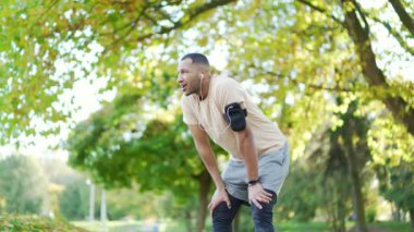 Erkek sporcu, parkta yoğun koşu seansından sonra ara verip kulaklıkla müzik dinlemekten hoşlanıyor. Fitness, genç bir adamın yoğun antrenmanında son derece çaba sarf etmesi.