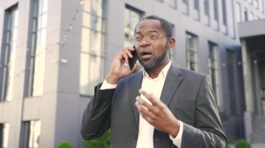 Afro-Amerikalı bir adam ofis binasının dışındaki telefon görüşmesinde hayal kırıklığını dile getiriyor. Profesyonel erkek, şehir ortamında akıllı telefondan iletişim kurarken öfke gösteriyor. Kızgın patron.